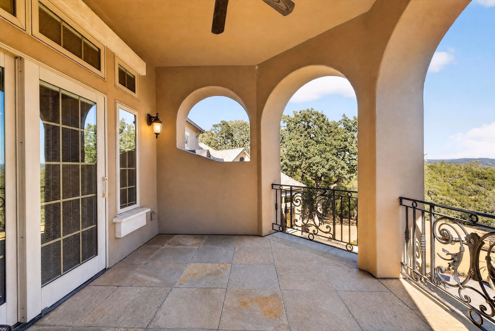 A covered upper balcony, with an arched opening, a wrought-iron rail and oak canopy beyond.