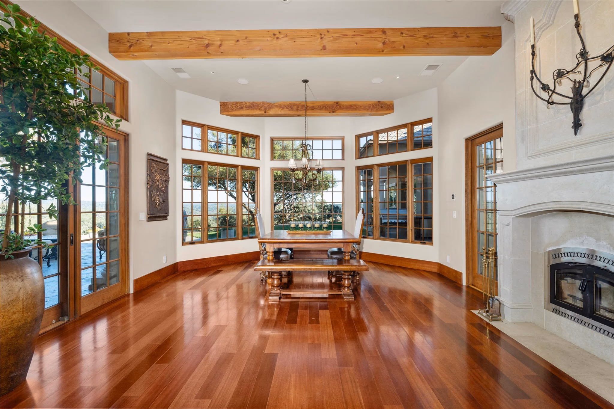 The breakfast room, a bay of windows around a long table, with a stone fireplace to one side and cherry floors.