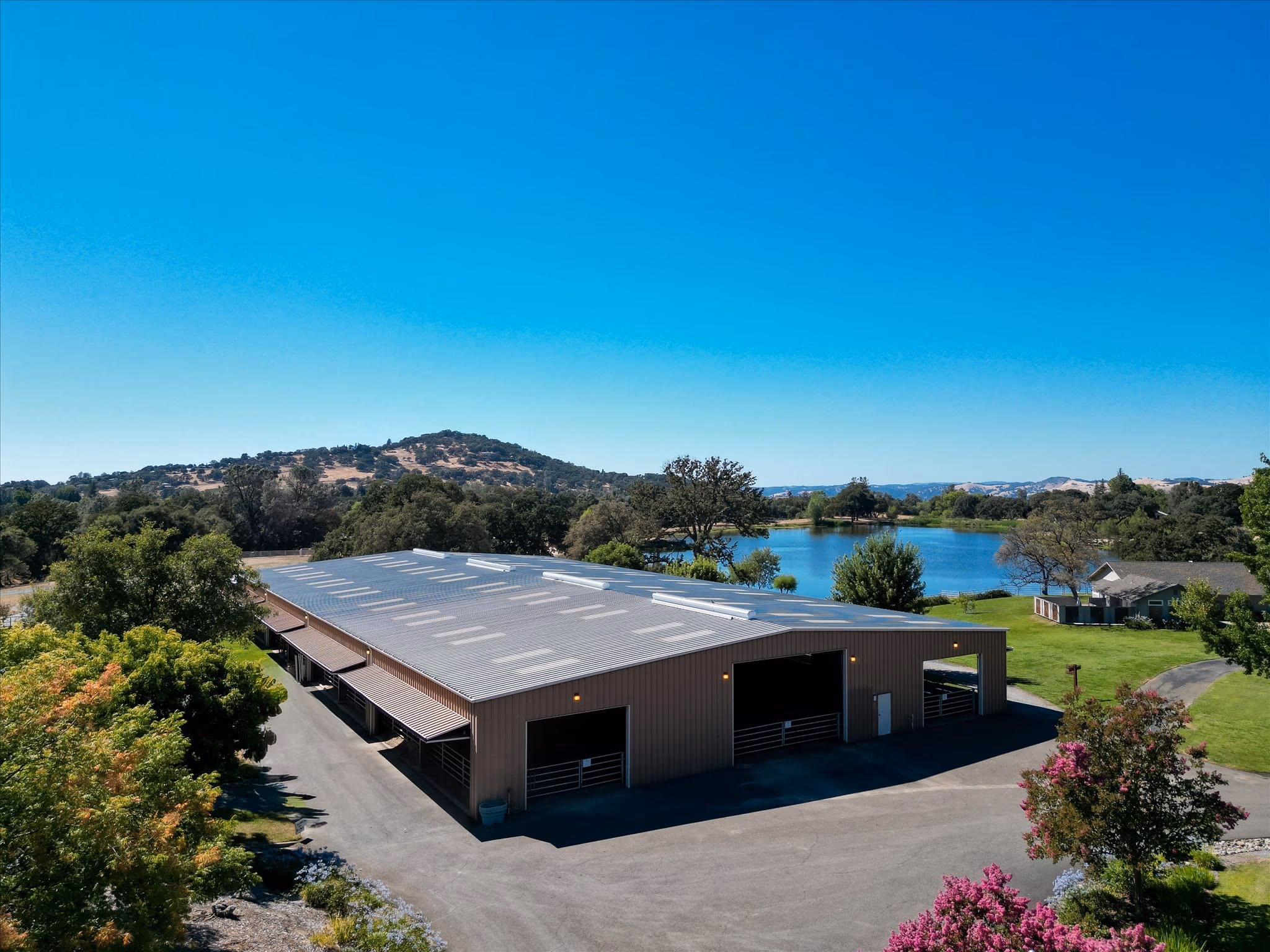 The covered riding arena from the air, a long clear-span roof with the private lake immediately behind it.