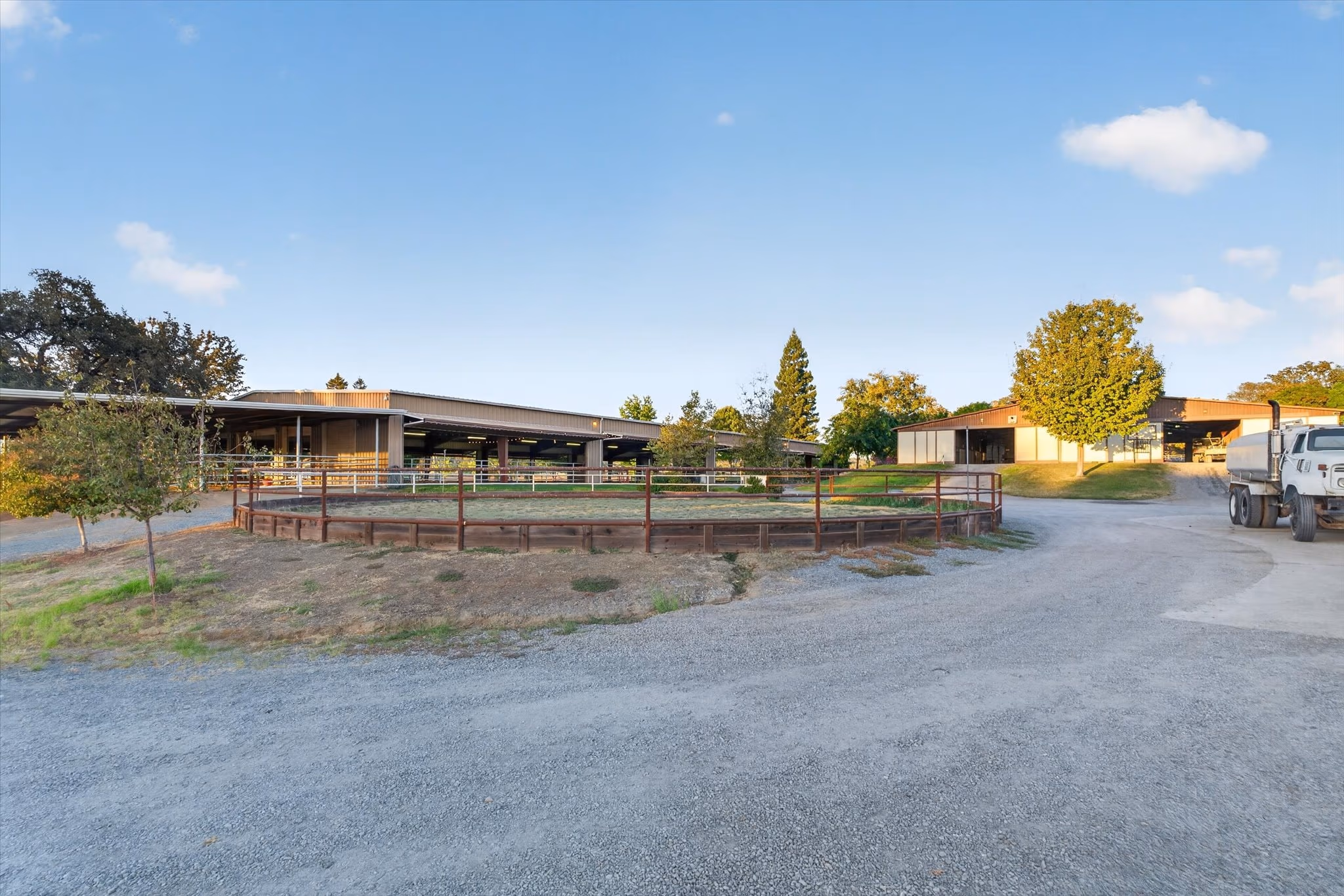 The service drive through the equestrian facility, with pipe-fenced turnouts on one side and the barns on the other.
