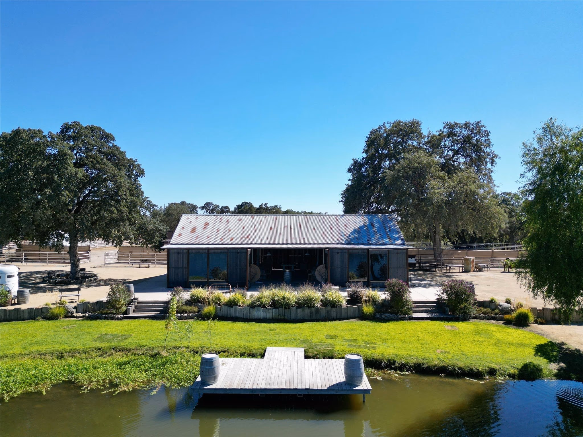The event barn, a restored barn with a corrugated roof and glazed openings, reflected in the water with a timber dock in the foreground.
