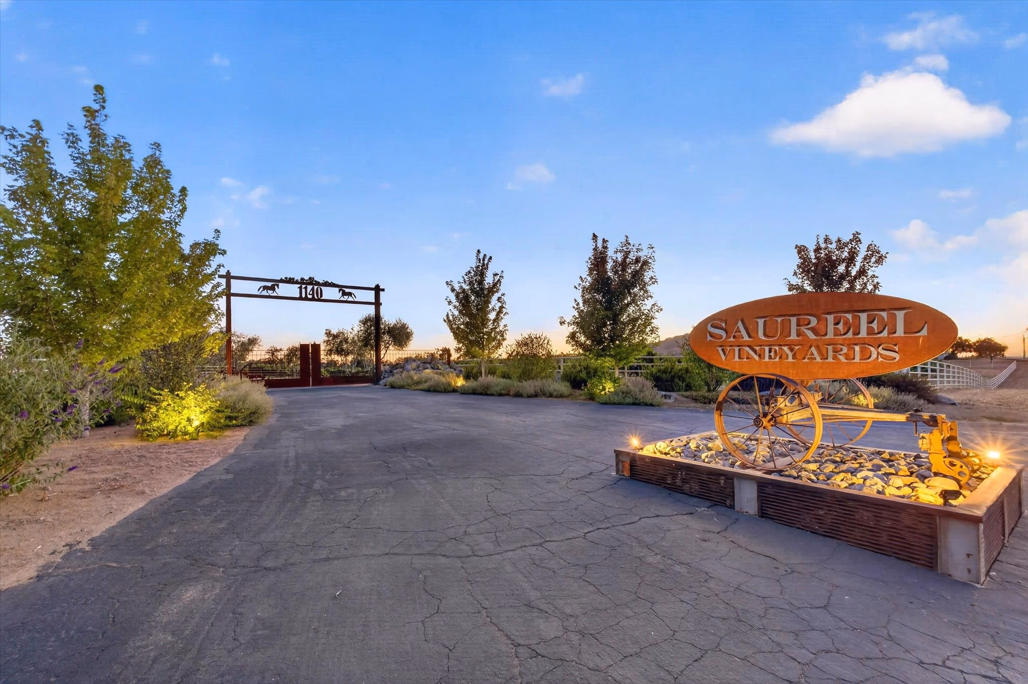 The Saureel Vineyards entrance sign, a steel and timber structure with a cut-metal horse motif, lit at dusk beside the drive.