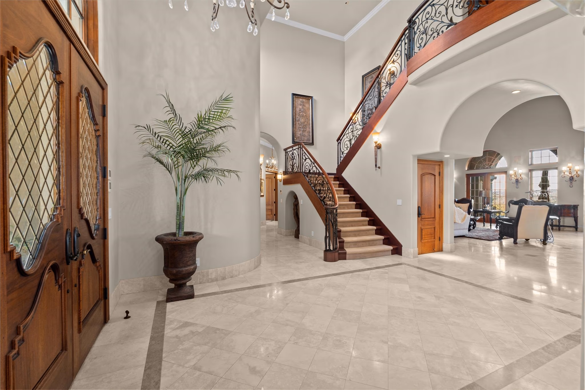 The entry hall of the main residence, with marble floors, a curved staircase with wrought-iron balustrade and leaded double doors standing open.