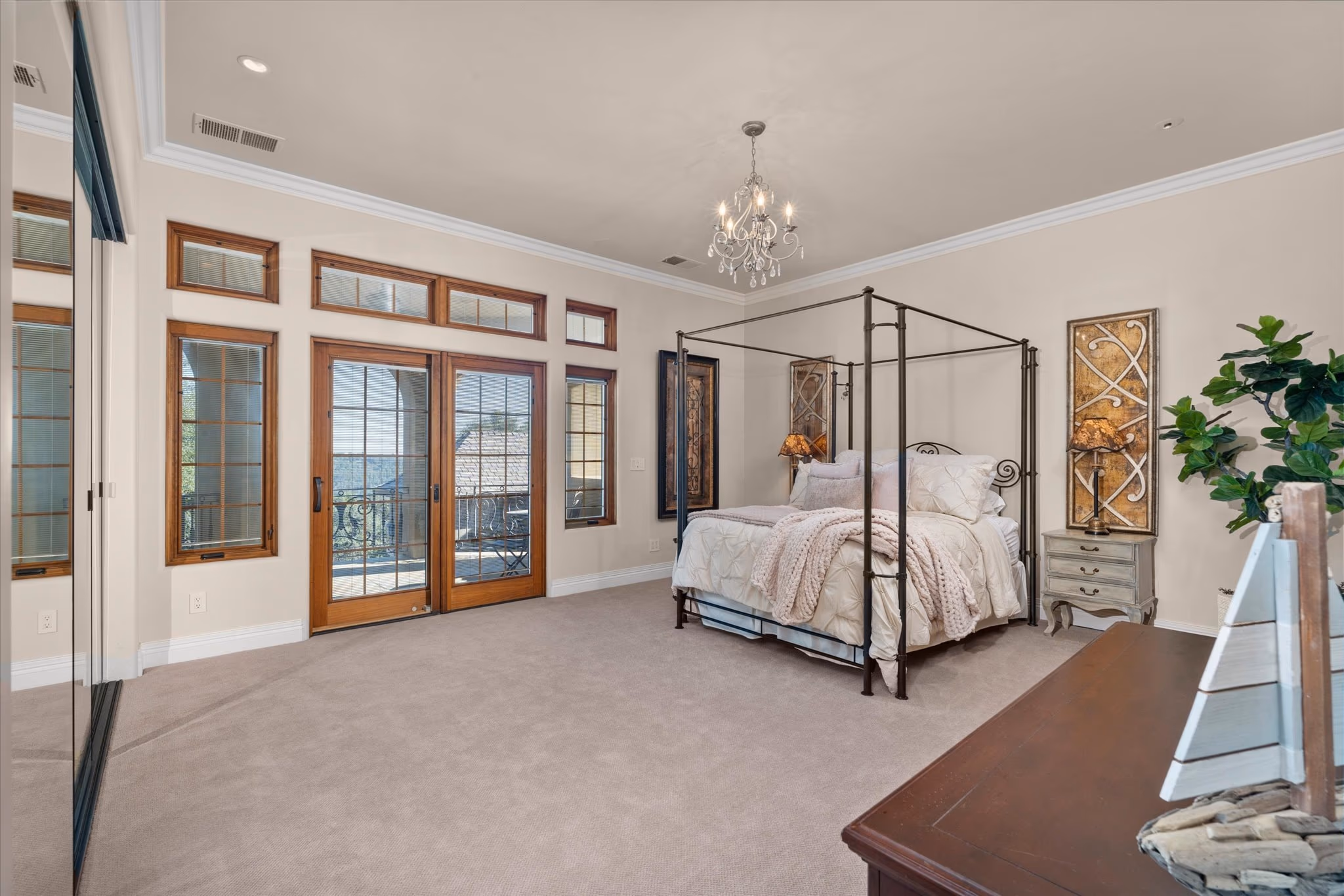 A guest bedroom, with an iron canopy bed, a chandelier and French doors opening onto a balcony.