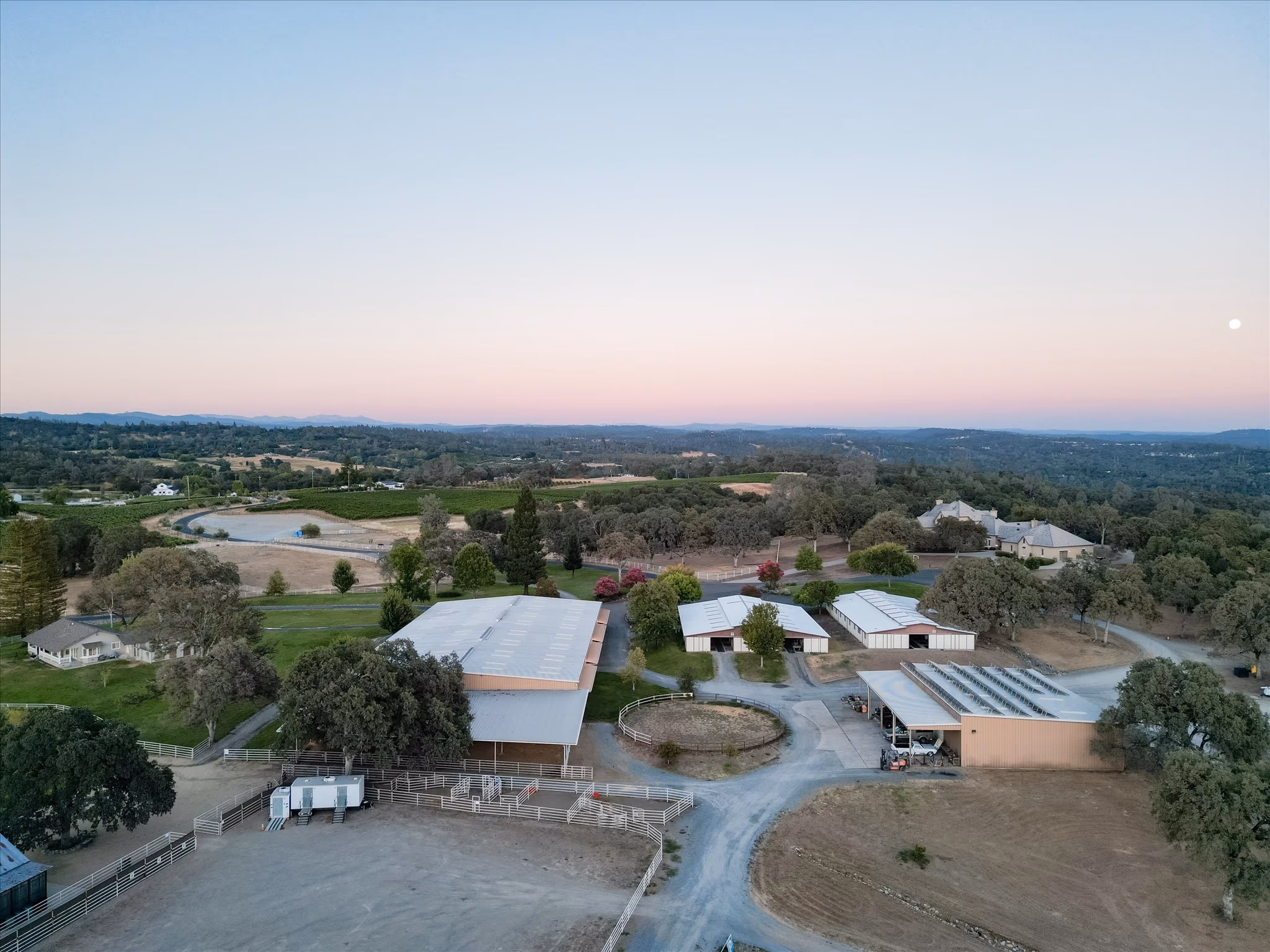The paddocks at dusk from the air,, round pen and pipe-fenced turnouts.