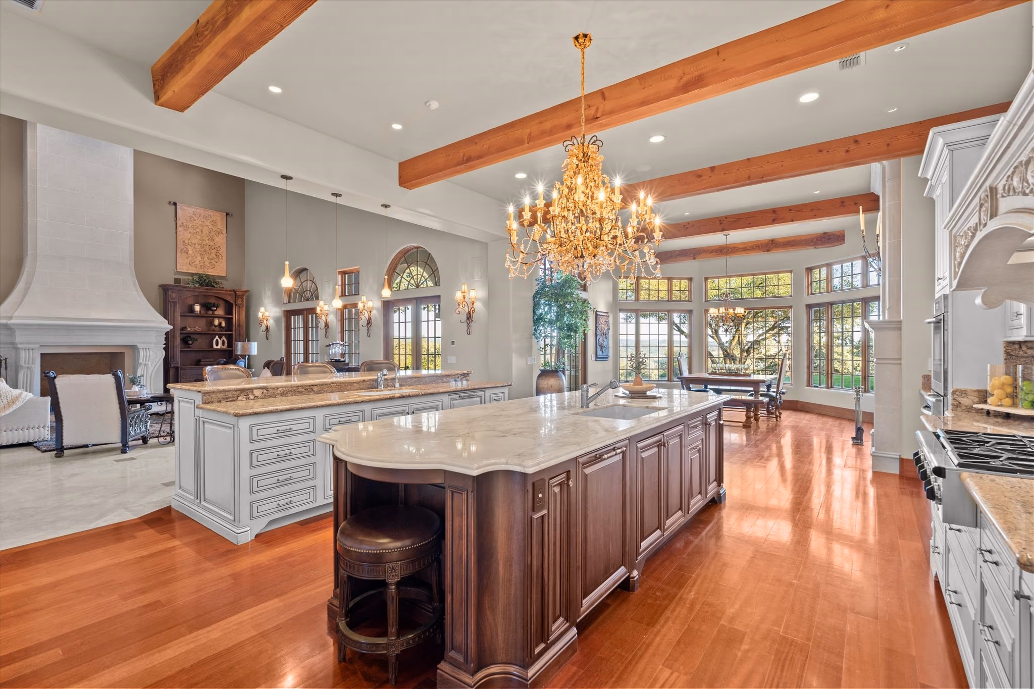 The walnut kitchen island under a beamed ceiling, with stone counters, a chandelier and windows to the grounds.