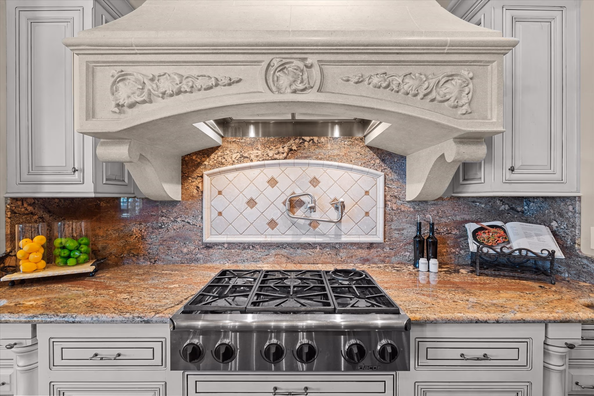 The carved limestone range hood over a professional gas range in the kitchen, with a tiled stone backsplash.