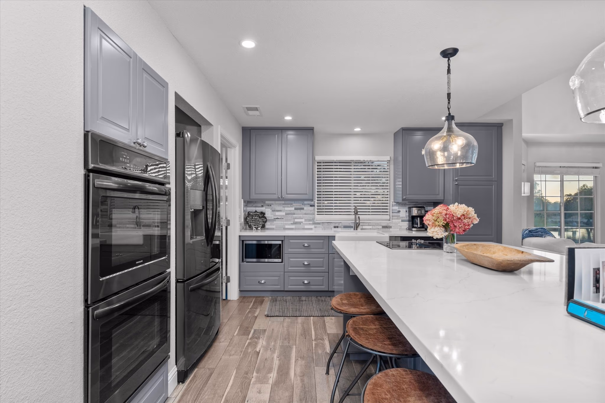 The kitchen of the lake house, with gray cabinetry, a white quartz island and stainless double ovens.