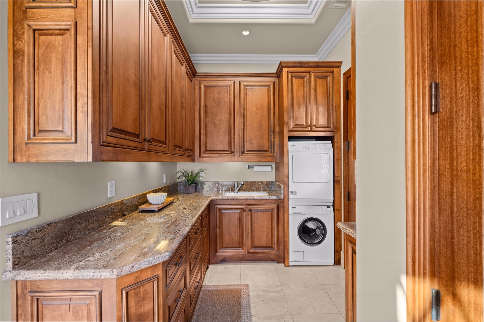 The laundry room, fitted in cherry cabinetry with a stone counter and a stacked washer and dryer.