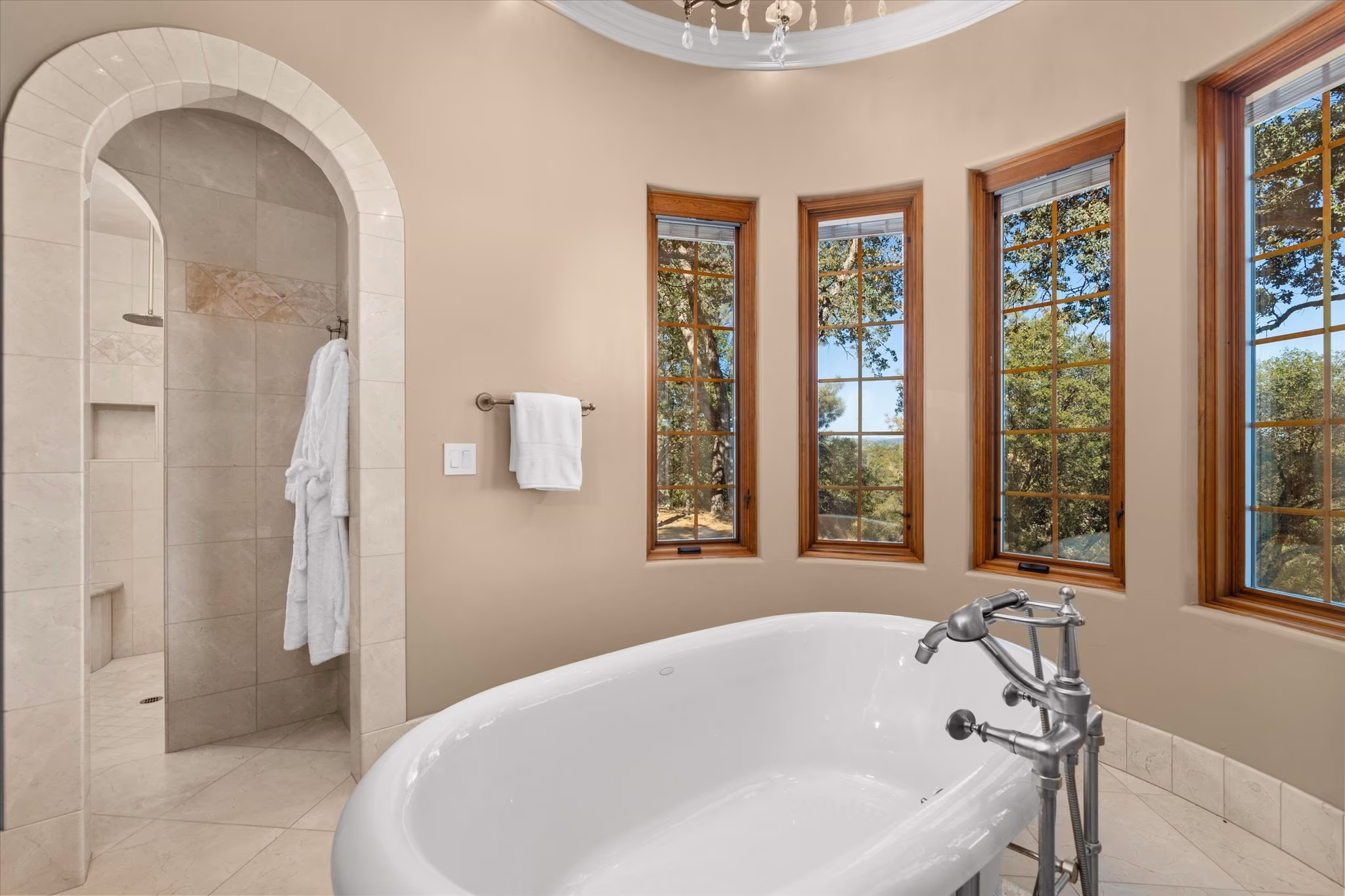 A freestanding roll-top bath set into a bay of windows in the primary bathroom, beside an arched walk-in shower.