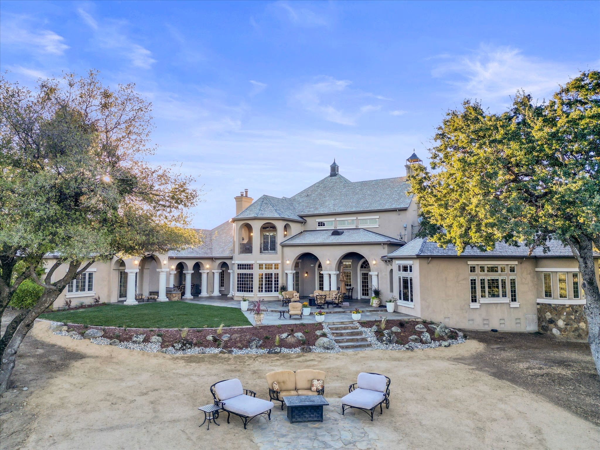 The rear elevation of the main residence, with a columned arcade, a second-floor loggia, lawn and a flagstone terrace.