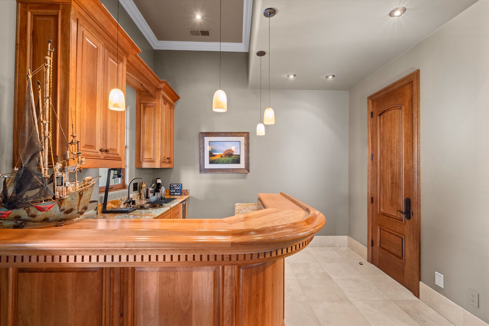 The curved timber wet bar, with a stone counter, pendant lighting and cabinetry behind.